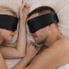Par som sover vendt mot hverandre med svarte Sovemaske Pro i silke for rolig søvn uten lysforstyrrelser