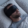 Mann sover med svart silkesovemaske som holder samme bredde hele veien rundt hodet
