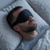 Mann sover med svart 3D sovemaske, den brede stroppen ligger flatt mot hodet